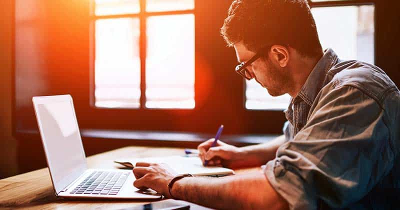 Man working on laptop and writing notes on paper