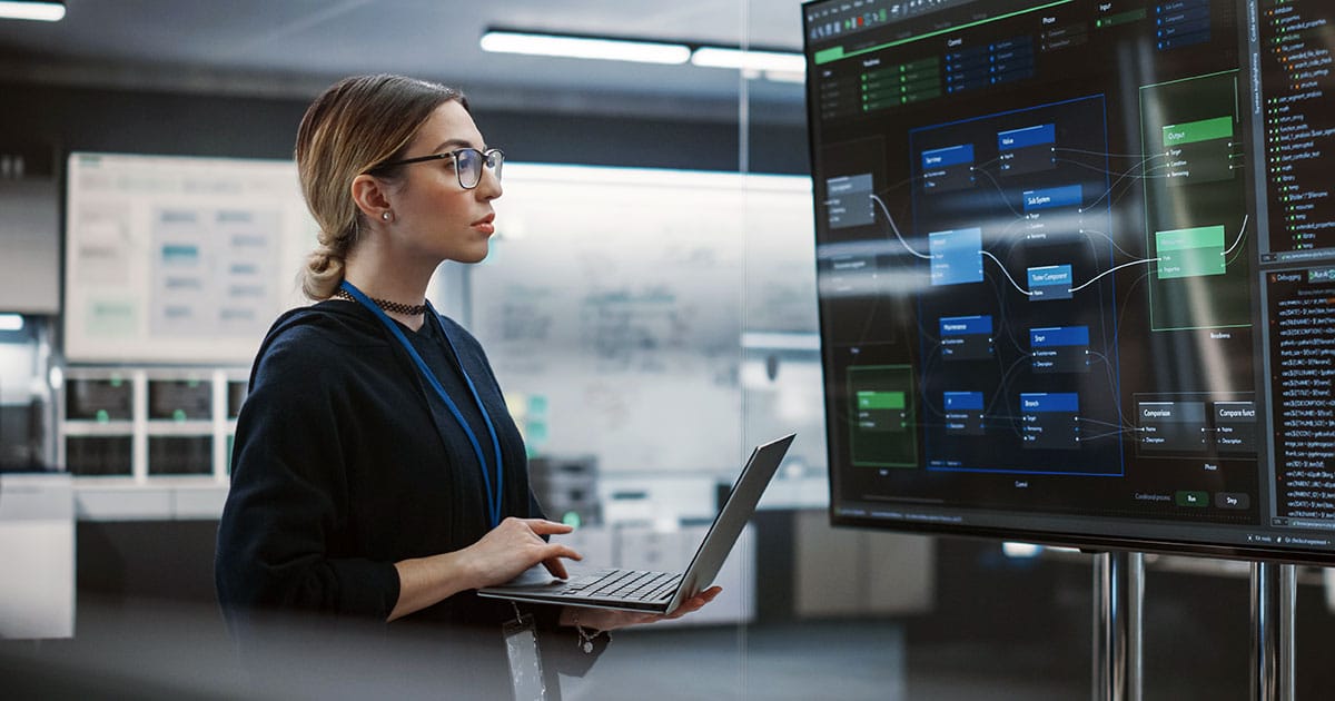 Female technology professional using laptop and large screen