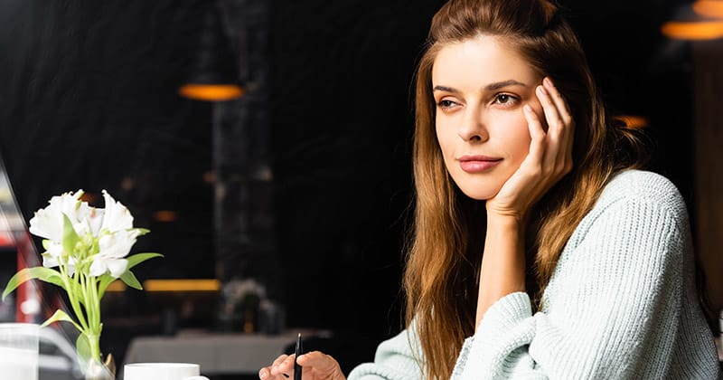 Woman sitting at table with coffee and pen thinking