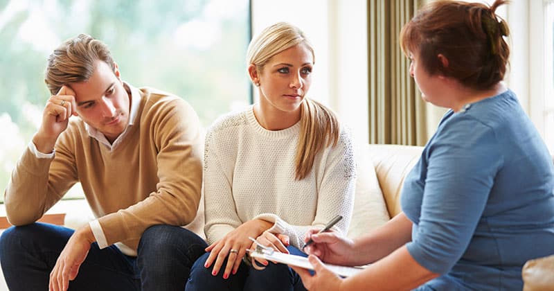 Woman sitting on a lounge suite with a couple and taking notes